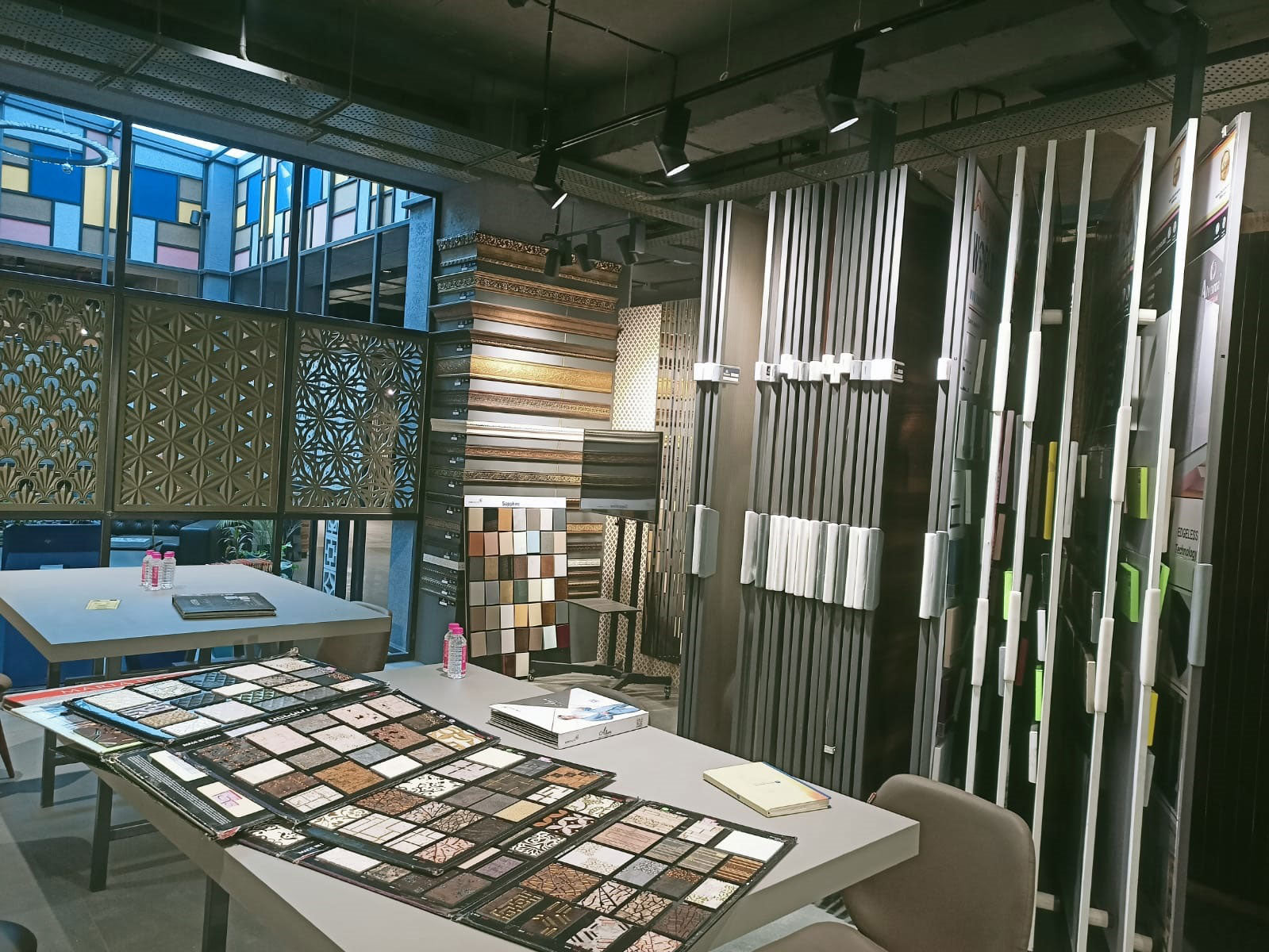 Brown wood grain louvers with textured finish displayed on wall and various interior design samples on tables in showroom