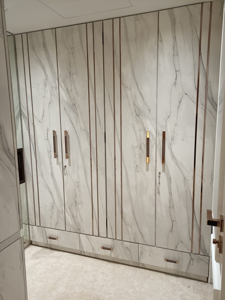 White marble laminate wall with vertical strips and gold handles in a modern interior design setting, matte finish visible.