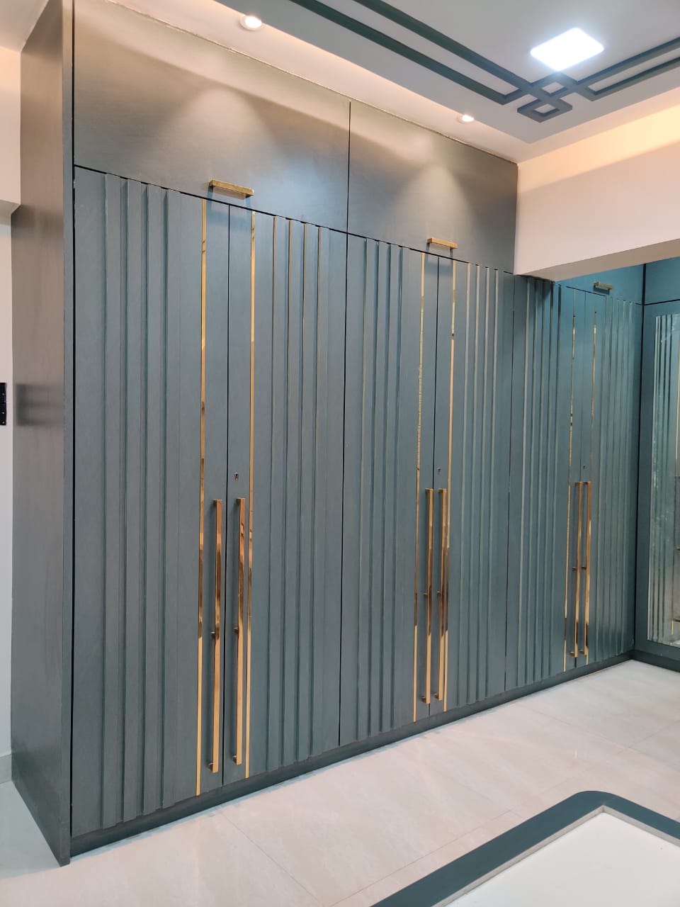 Matte grey laminate wall with vertical grooves and gold handles in a modern interior setting with recessed lighting
