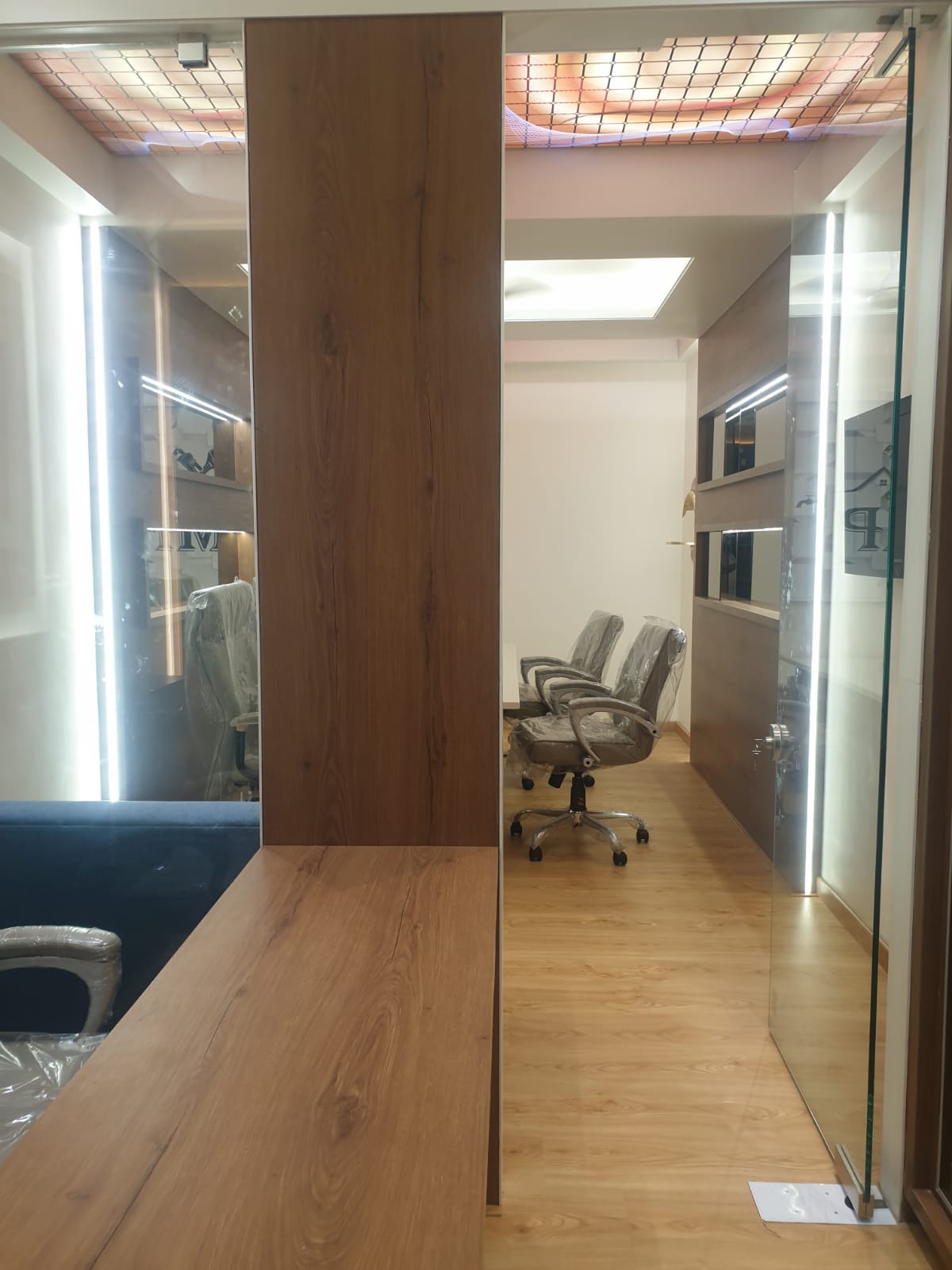 Wood grain laminate wall and floor in office space with glass doors and modern furniture, showing matte finish and wood