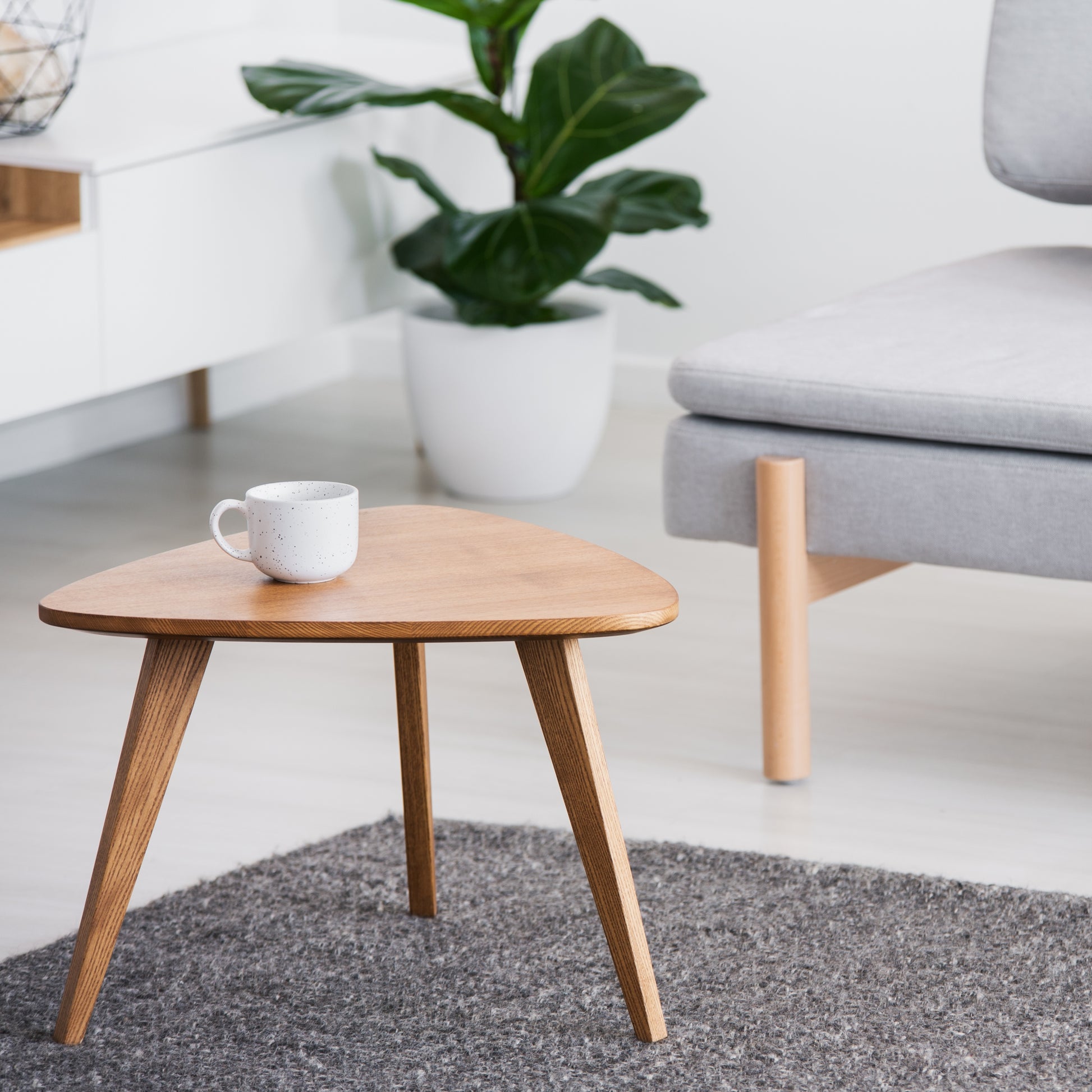 Wooden side table with matte finish and visible wood grain in a modern living room setting with gray furniture and decor.