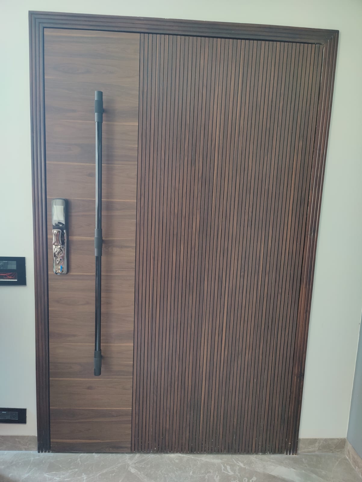 Brown wood laminate door with matte finish and vertical slats, featuring a long handle and installed in a white wall.