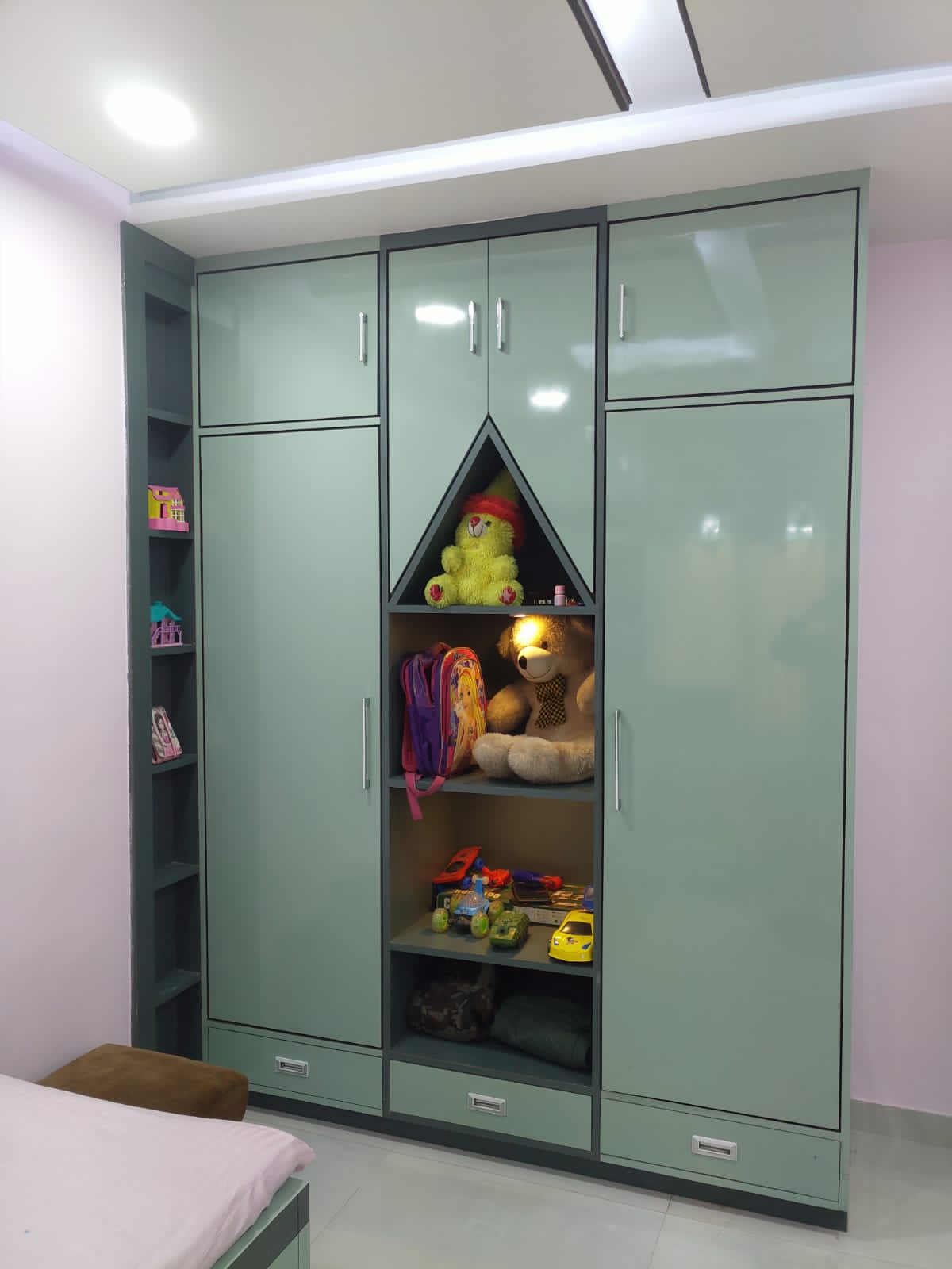Glossy green laminate cabinet doors with silver handles in a child's bedroom with toys and stuffed animals inside.