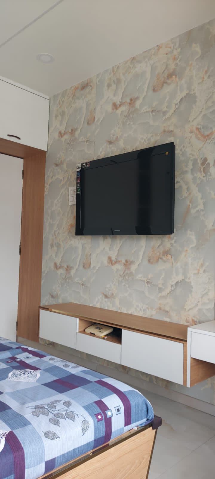 Multicolour marble laminate wall with matte finish and veining pattern in a modern bedroom with mounted TV and furniture