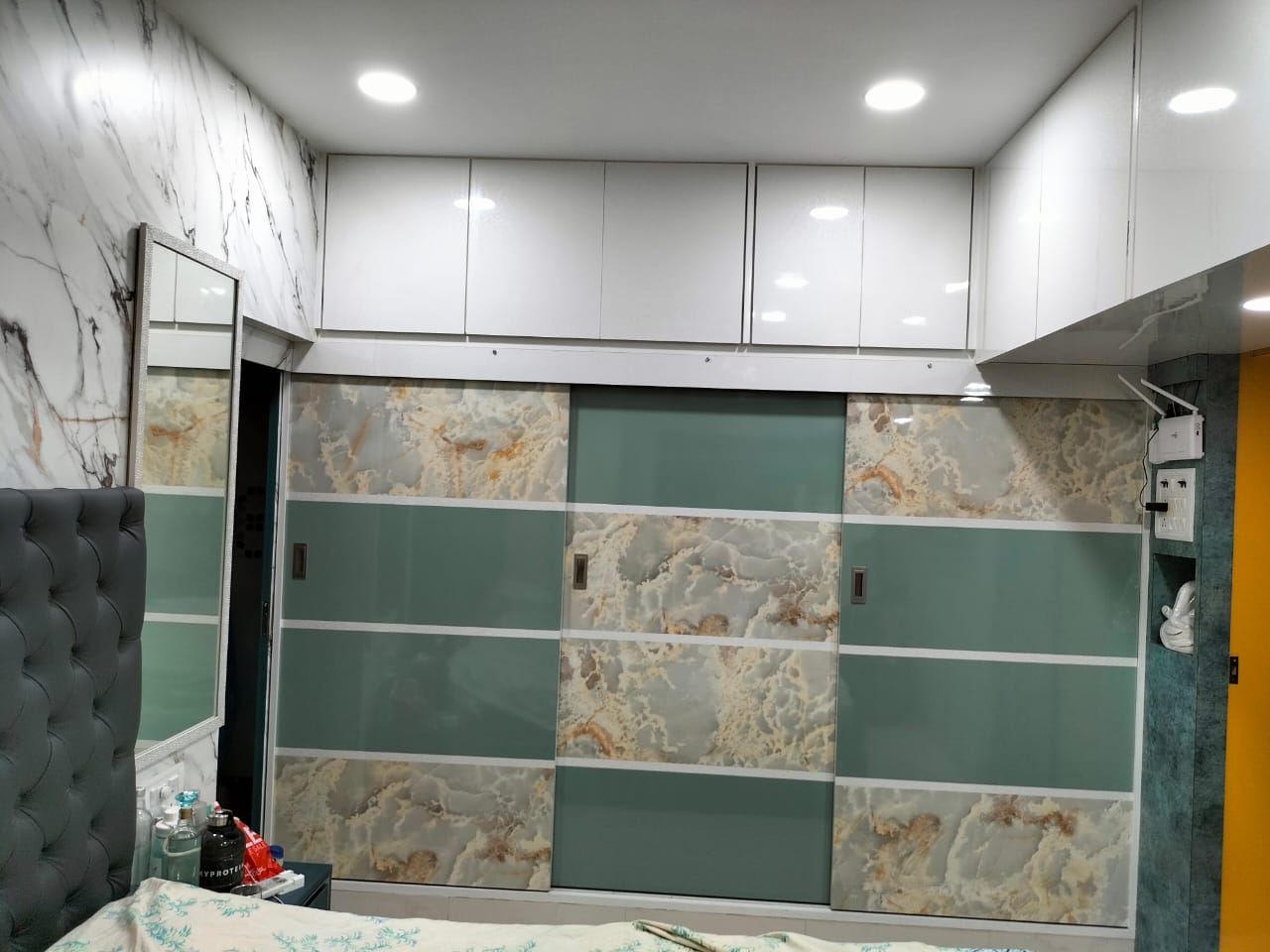 Marble laminate wardrobe with matte finish and white cabinets in a bedroom with marble patterned walls