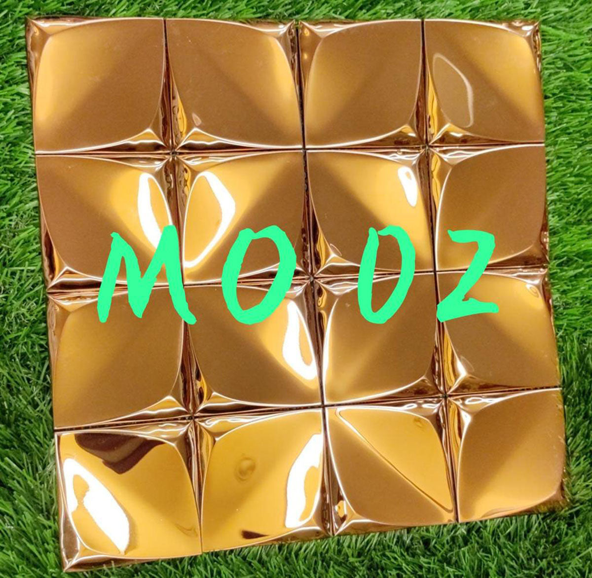 Gold designer louver panel with shiny textured surface and pyramid pattern, arranged in grid formation on green grass