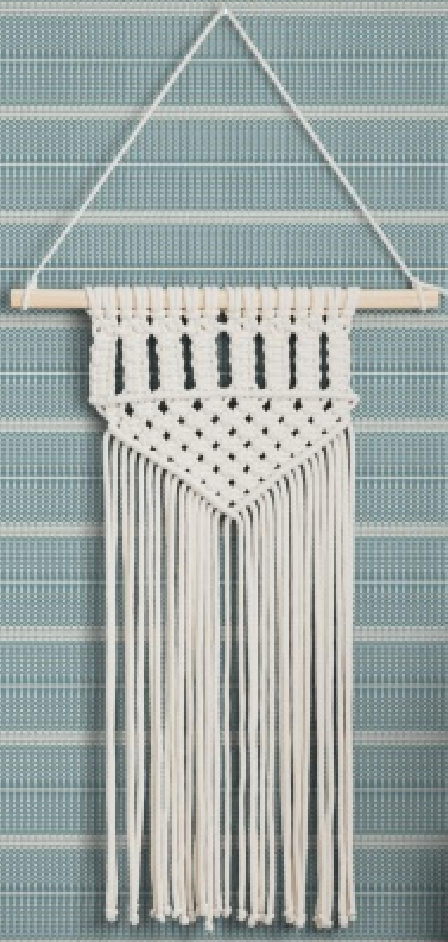 White macrame wall hanging with fringe on matte laminate wall panel background.