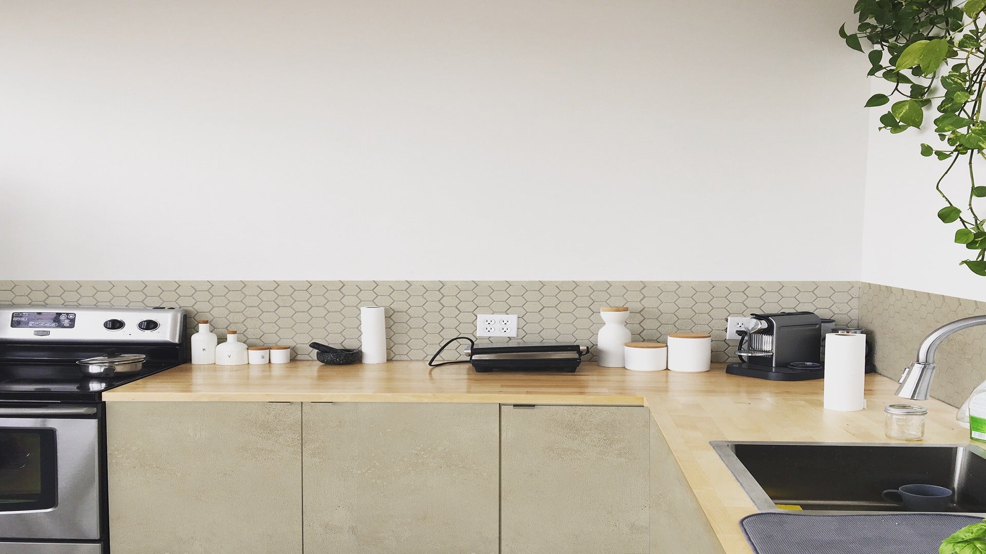 Beige hexagonal tile backsplash in modern kitchen with wooden countertop and stainless steel appliances and sink area.