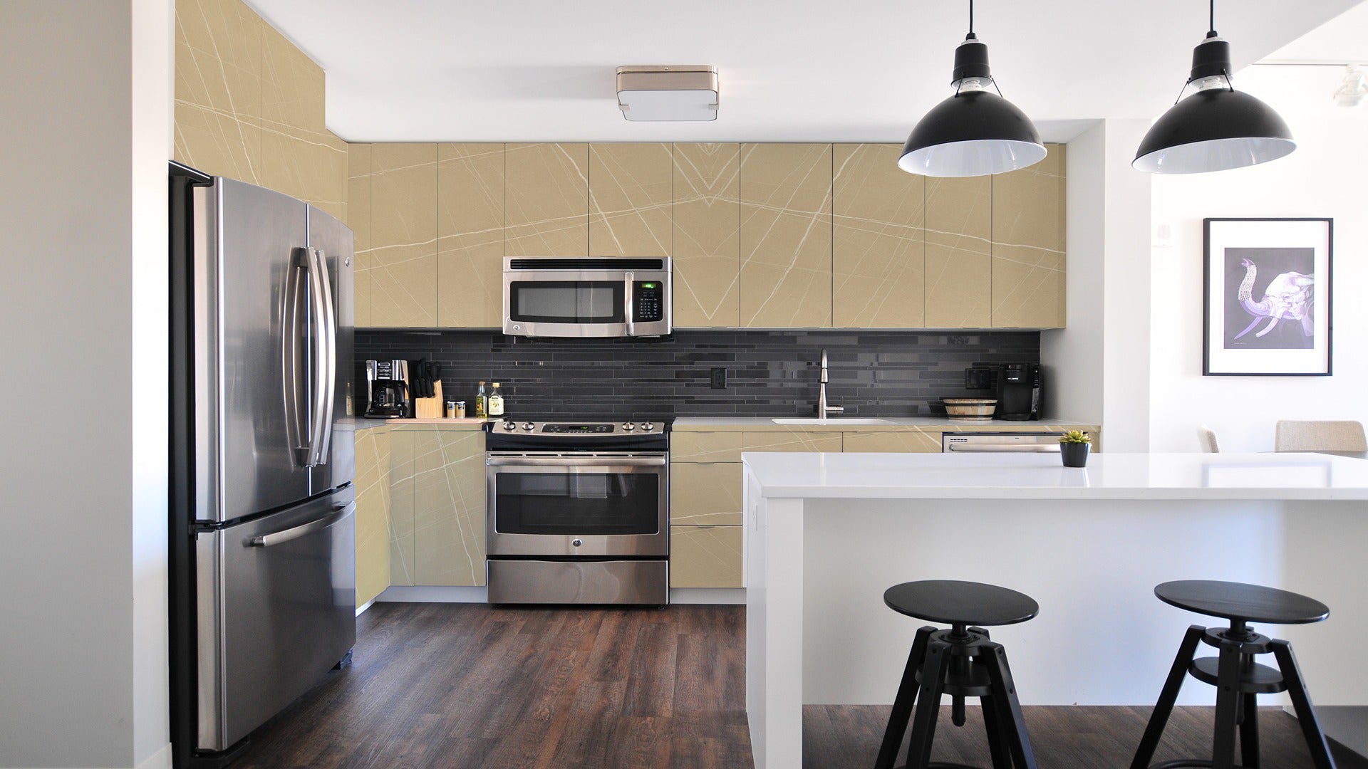 Beige marble laminate kitchen cabinets with white veining and glossy finish, paired with stainless steel appliances and dark