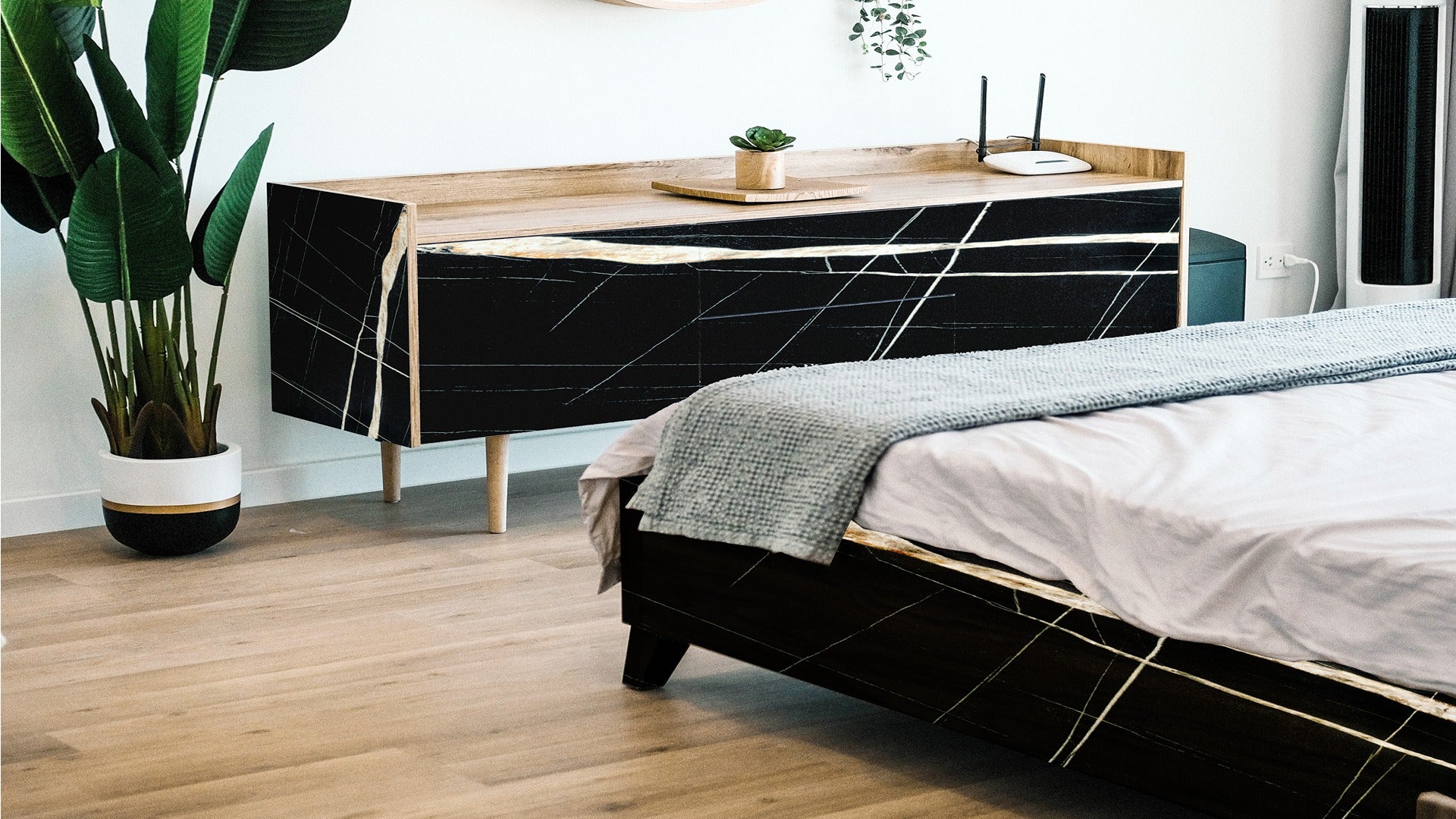 Black marble patterned laminate furniture in modern bedroom with wooden accents and green plants, showing glossy finish and
