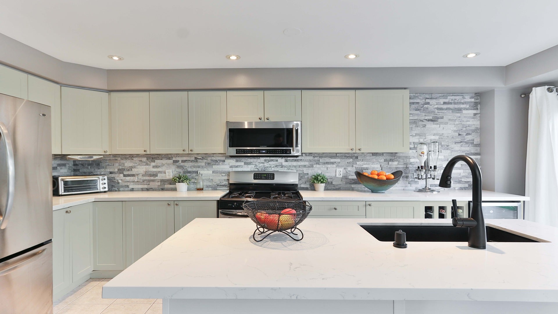 Matte grey laminate kitchen cabinets and grey stone backsplash in a modern kitchen with white countertops and stainless