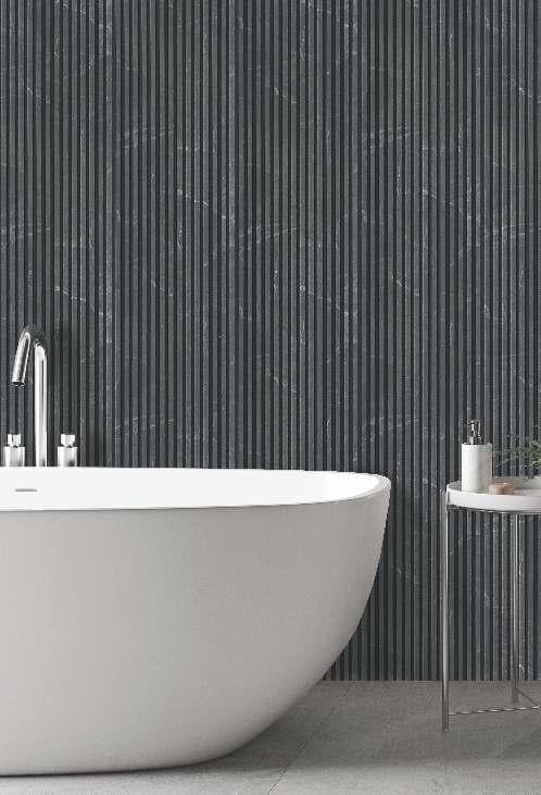 Grey marble louver wall with white veining and vertical slats behind a white bathtub and small side table